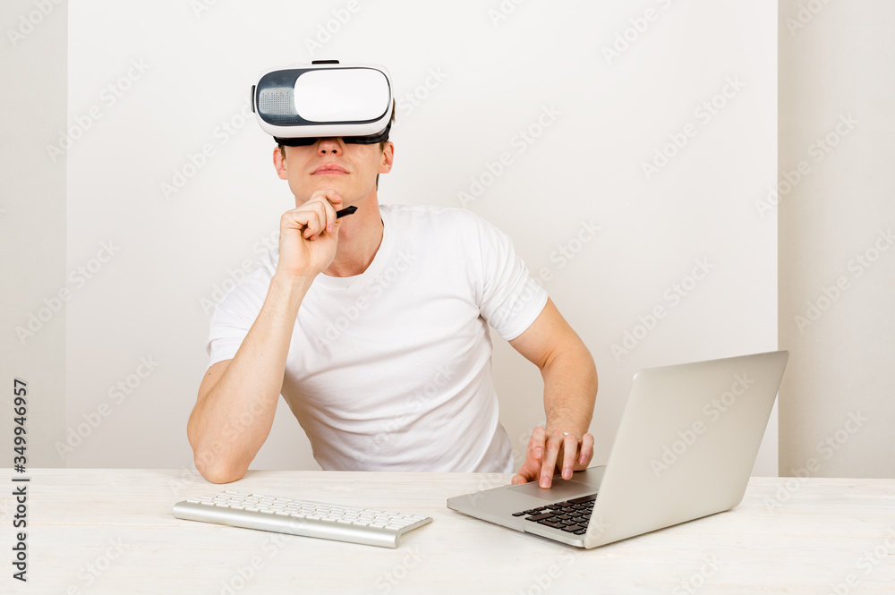 Male using virtual reality headset interacts with augmented things orienting in three dimensional space while sitting on his desk with keyboard and laptop on white background. Male using virtual reality headset interacts with augmented things orienting in three dimensional space while sitting on his desk with keyboard and laptop on white background.