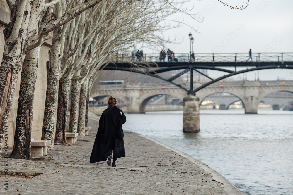 A woman in a black coat is walking along the Seine embankment. A woman in a black coat is walking along the Seine embankment.