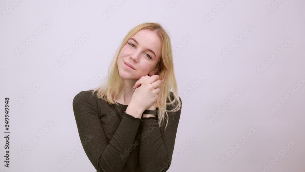 Young Blonde Woman In Black Sweater With Stylish Watch On White Background, Cute Girl Holds Hands Together Near Her Face, Looks Friendly With Love. The Concept Innocence And Tenderness Of People Young Blonde Woman In Black Sweater With Stylish Watch On White Background, Cute Girl Holds Hands Together Near Her Face, Looks Friendly With Love. The Concept Innocence And Tenderness Of People