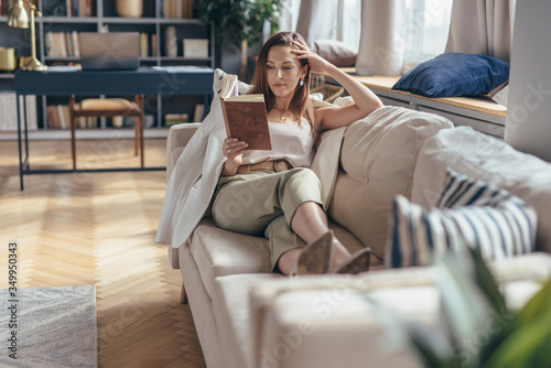 Woman lying on sofa and reading book at home