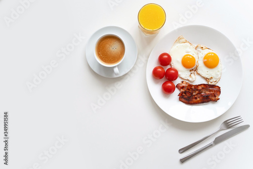 Classic breakfast with two eggs, bacon, fresh tomatoes, black coffee and fresh orange juice on the white table. Copy space. Top view.