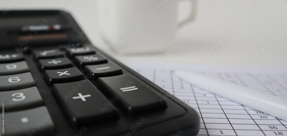 A white pen lies near the black calculator. A white cup is standing nearby. Close-up, banner. A white pen lies near the black calculator. A white cup is standing nearby. Close-up, banner.