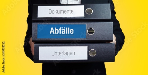 Abfälle. Anwalt im Anzug trägt einen Stapel Ordner. 3 Aktenordner. Blaue Beschriftung mit Text. Hintergrund gelb. Recht, Gesetz, Rechtsprechung