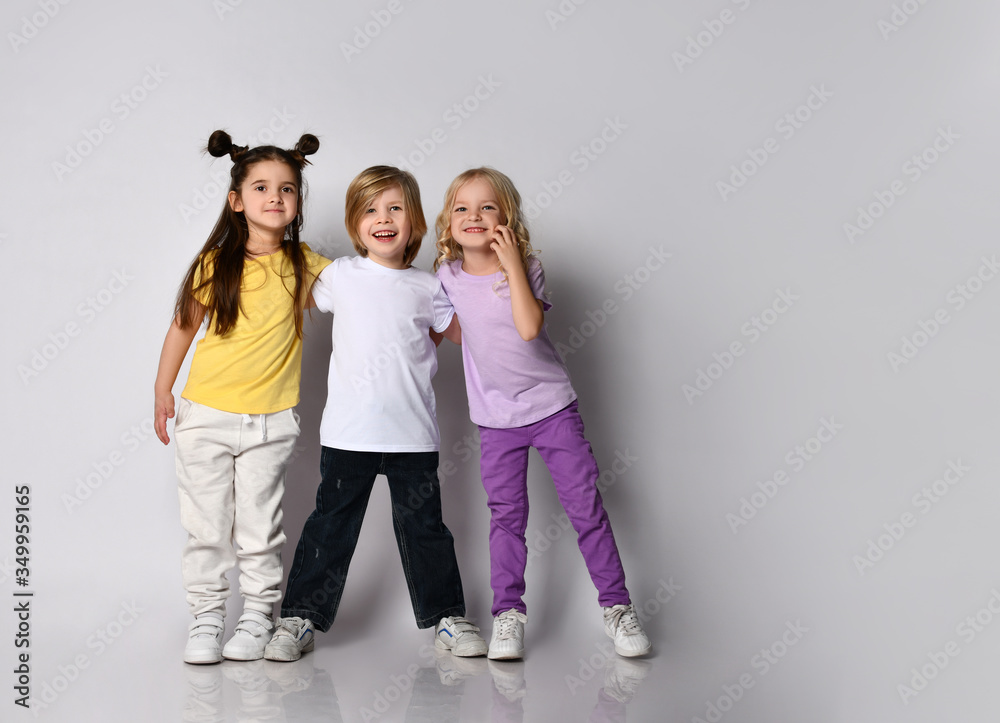 Obraz premium Little boy and girls dressed in colorful casual clothes. They are smiling and hugging each other, posing isolated on white