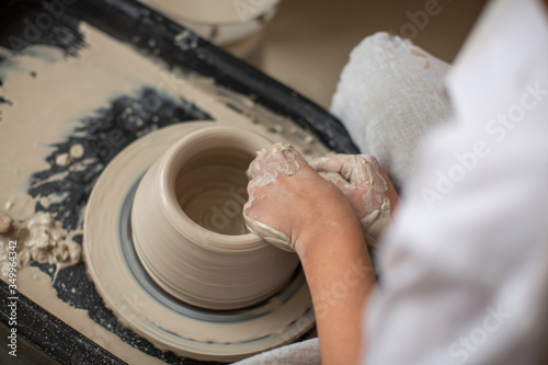 The hands of a professional who creates a pot of clay on a potter's wheel. Close-up, top view. Pottery workshop, process of work.