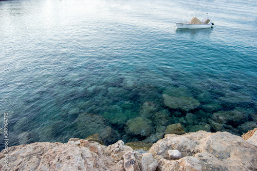 Small boat on the clear blue water of a calm sea near a rocky shore