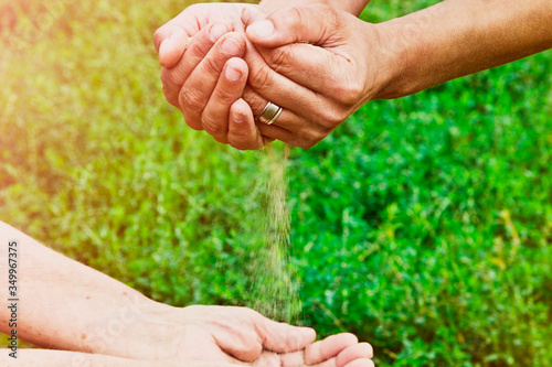 Sand filling grandmother's old palms close-up. Loose sand from young to old hands. Hourglass in the hands of an old grandmother close-up. Youth and old age conceptual photo. Grandmother and granddaugh