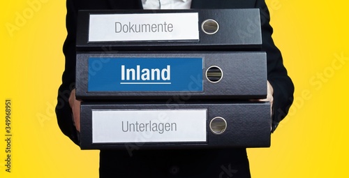 Inland. Anwalt im Anzug trägt einen Stapel Ordner. 3 Aktenordner. Blaue Beschriftung mit Text. Hintergrund gelb. Recht, Gesetz, Rechtsprechung