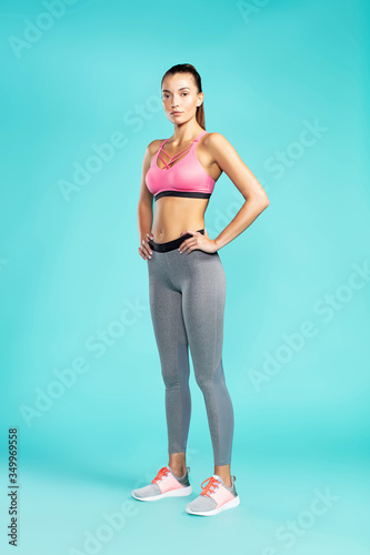 Ready for workout. Full length of young beautiful woman in sportswear looking at camera while standing against blue background. Sport and fitness