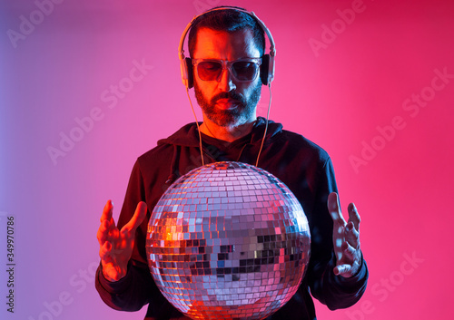 Colorful studio portrait of a bearded deejay with headphones and sunglasses against red and blues background.