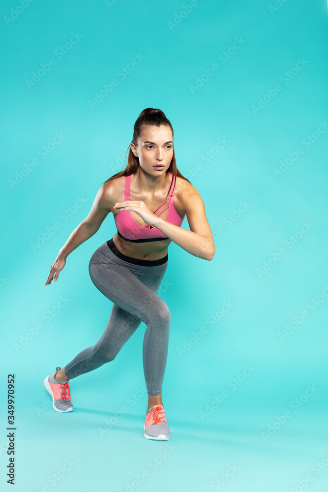 Fototapeta premium Workout. Full length of young attractive woman in sportswear exercising while standing against blue background
