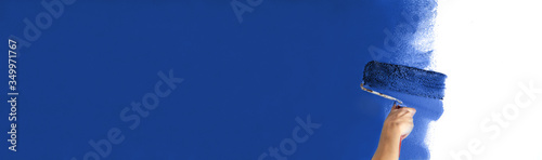 Wallpaper Mural Human hand with large roller of paint begins to paint a white wall handicraft education contrast color sample color test tool renovation dark blue strong blue water Torontodigital.ca