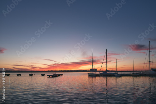 Landscape of evening yacht club right after sunset. Silhouettes of yachts and boats at the horizon. Dramatic and vibrant evening sky © AlexGo