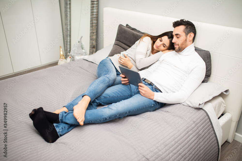 Couple watching a movie on their tablet while on the bed - obrazy, fototapety, plakaty 