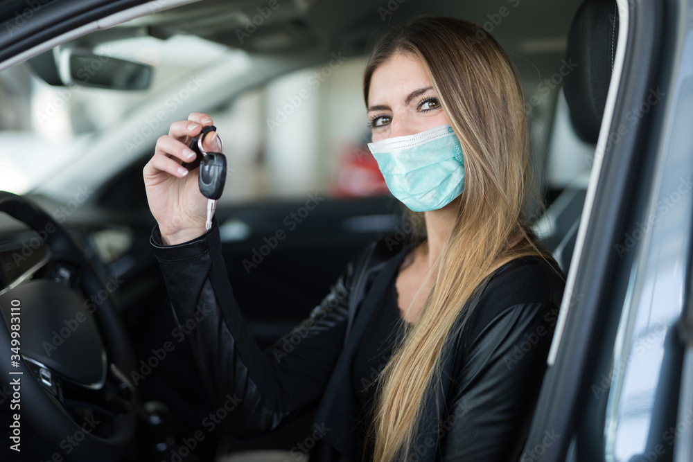 Masked woman showing the key of her new car in a car dealer saloon - obrazy, fototapety, plakaty 
