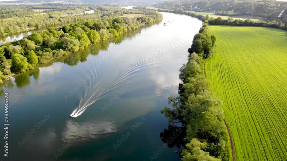 Scenic aerial view of the Seine river with boats and cargo barges and green fields in French countryside. Val d'Oise department, Ile-de-France, Northern France
