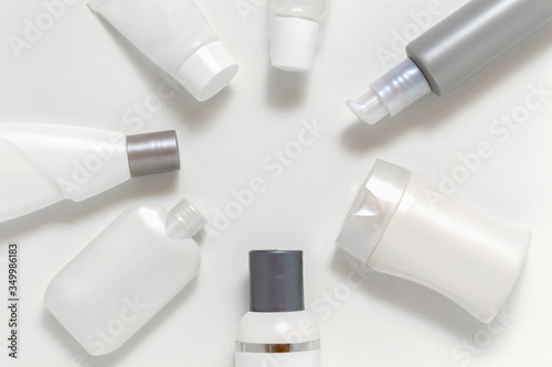 Cosmetic jars on a light background located around round copy space for text. Monochrome set of white and grey bottles