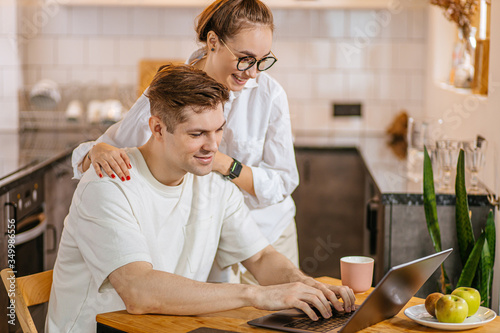 careful caucasian wife support her husband while he is working from home at freelance. hundsome guy sit with laptop, his lovely girlfriend support him and talk photo