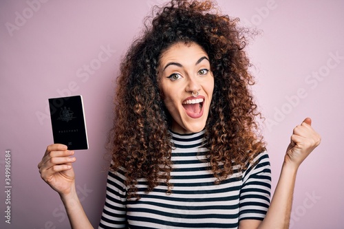 Beautiful tourist woman with curly hair and piercing holding australia australian passport id screaming proud and celebrating victory and success very excited, cheering emotion