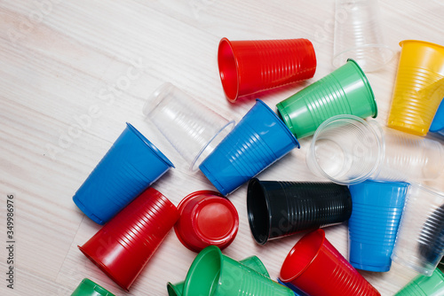A large pile of multicolored plastic cups scattered on the floor with free space. Pollution of the environment by human waste