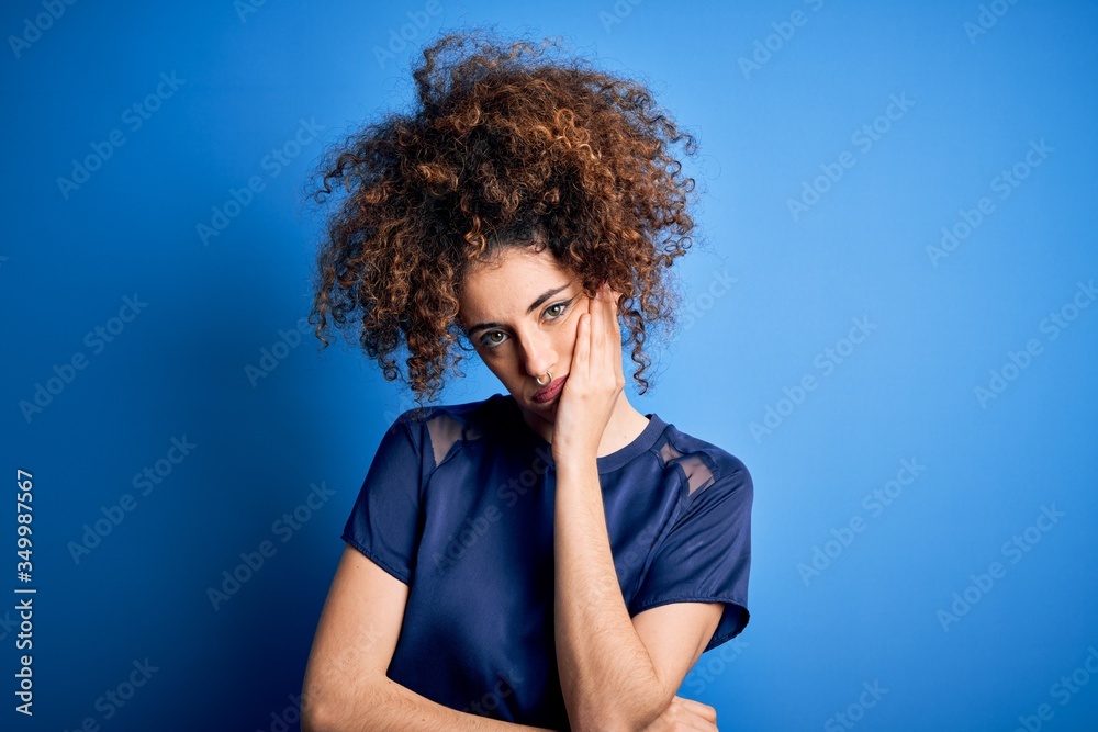 Young beautiful woman with curly hair and piercing wearing casual blue t-shirt thinking looking tired and bored with depression problems with crossed arms. Young beautiful woman with curly hair and piercing wearing casual blue t-shirt thinking looking tired and bored with depression problems with crossed arms.