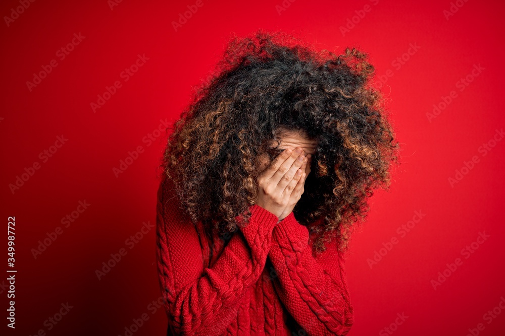 Young beautiful woman with curly hair and piercing wearing casual red sweater with sad expression covering face with hands while crying. Depression concept. Young beautiful woman with curly hair and piercing wearing casual red sweater with sad expression covering face with hands while crying. Depression concept.