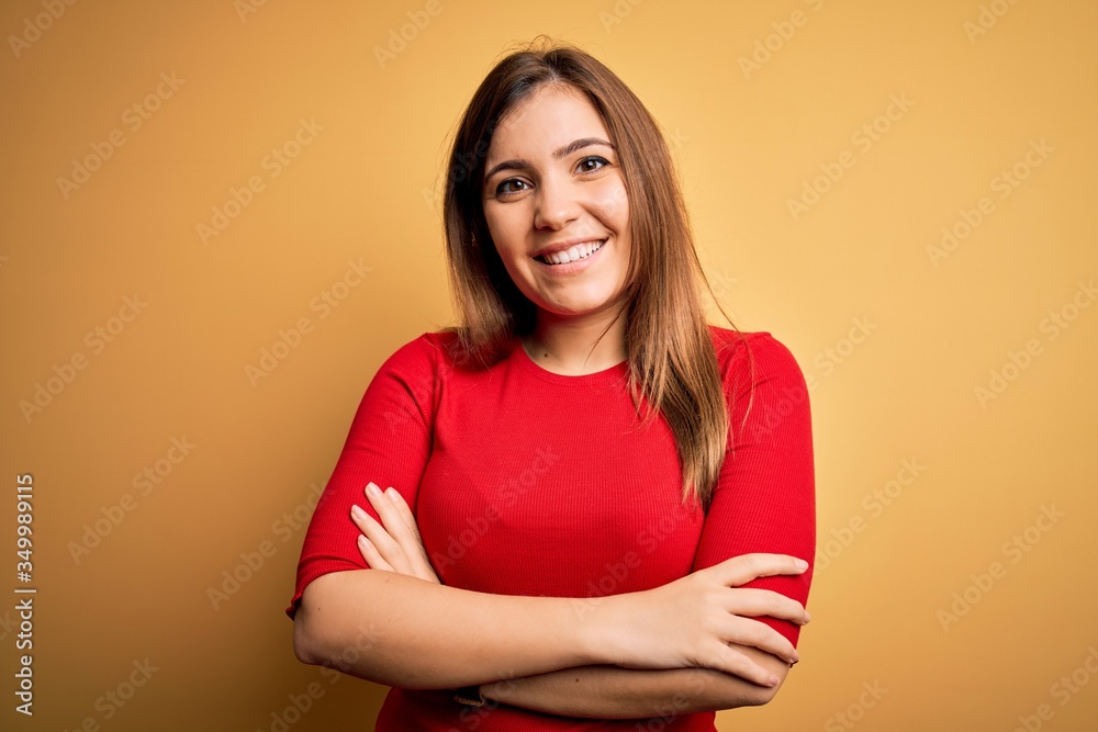 Beautiful young woman wearing casual red t-shirt over yellow isolated background happy face smiling with crossed arms looking at the camera. Positive person. Beautiful young woman wearing casual red t-shirt over yellow isolated background happy face smiling with crossed arms looking at the camera. Positive person.
