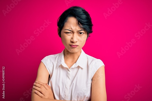 Young beautiful asian girl wearing casual summer shirt standing over isolated pink background skeptic and nervous, disapproving expression on face with crossed arms. Negative person.
