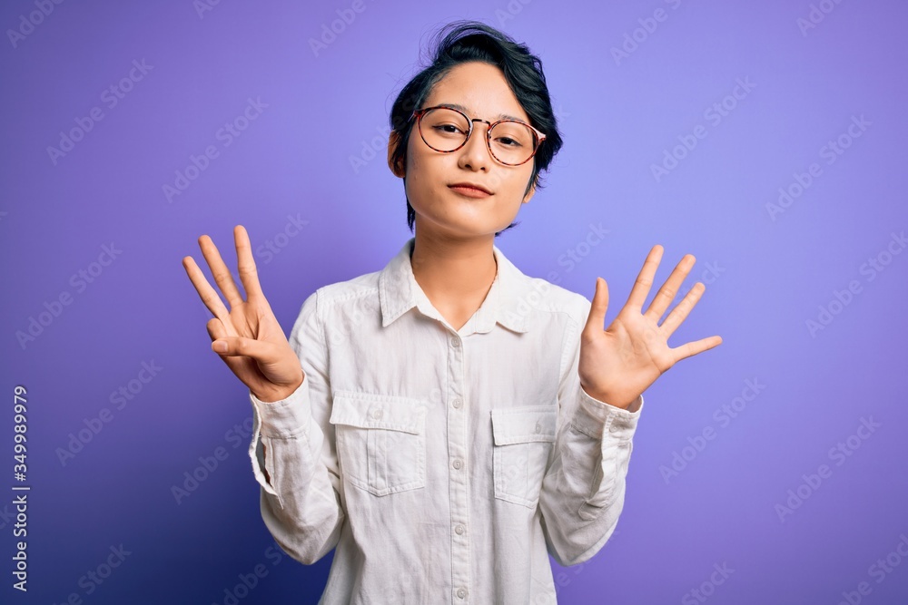Young beautiful asian girl wearing casual shirt and glasses standing over purple background showing and pointing up with fingers number eight while smiling confident and happy. Young beautiful asian girl wearing casual shirt and glasses standing over purple background showing and pointing up with fingers number eight while smiling confident and happy.