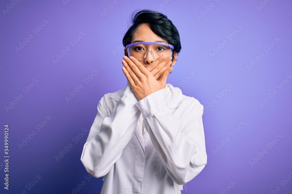 Young beautiful asian scientist girl wearing coat and glasses over purple background shocked covering mouth with hands for mistake. Secret concept.