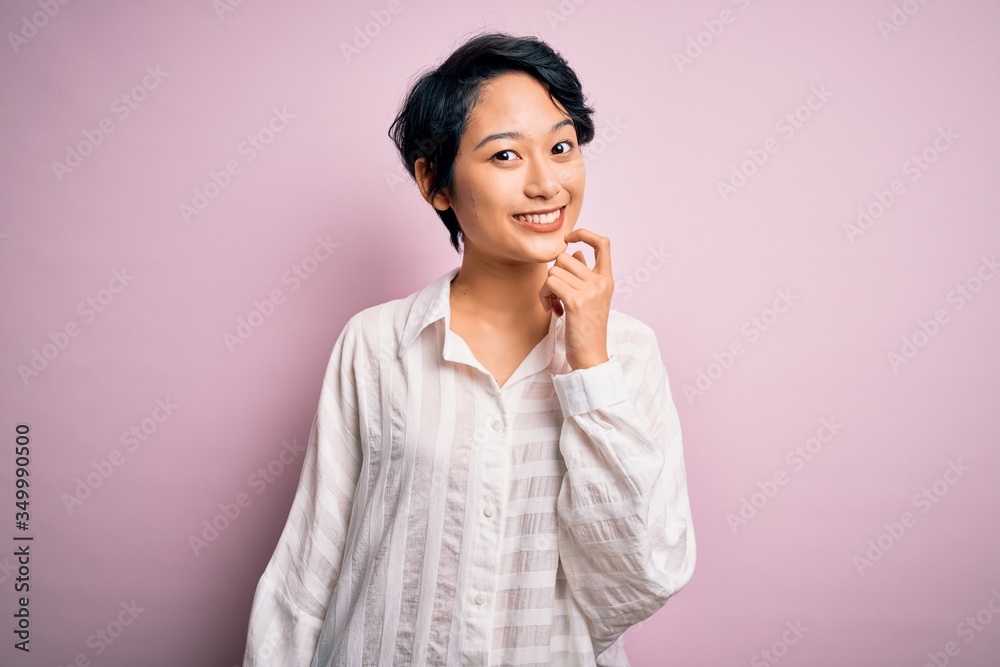 Young beautiful asian girl wearing casual shirt standing over isolated pink background looking confident at the camera smiling with crossed arms and hand raised on chin. Thinking positive. Young beautiful asian girl wearing casual shirt standing over isolated pink background looking confident at the camera smiling with crossed arms and hand raised on chin. Thinking positive.