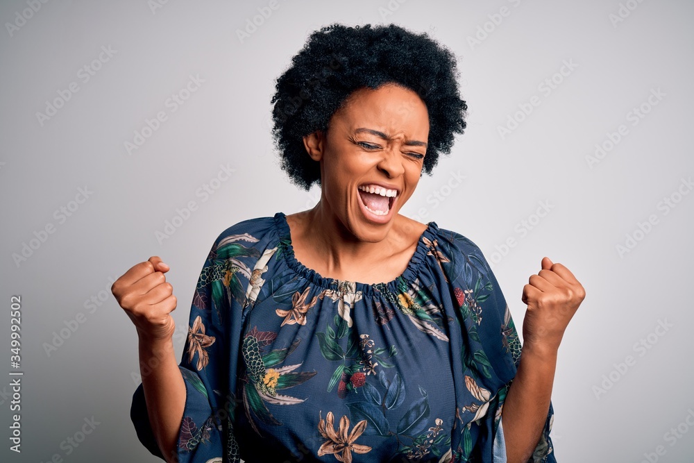 Young beautiful African American afro woman with curly hair wearing casual floral dress very happy and excited doing winner gesture with arms raised, smiling and screaming for success. Celebration
