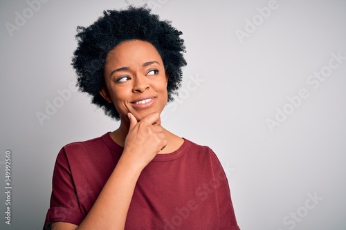 Young beautiful African American afro woman with curly hair wearing casual t-shirt standing with hand on chin thinking about question, pensive expression. Smiling with thoughtful face. Doubt concept. © Krakenimages.com