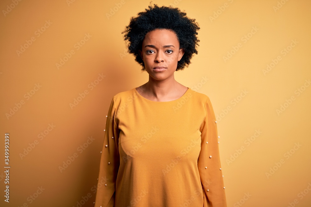 Young beautiful African American afro woman with curly hair wearing casual t-shirt with serious expression on face. Simple and natural looking at the camera. Young beautiful African American afro woman with curly hair wearing casual t-shirt with serious expression on face. Simple and natural looking at the camera.