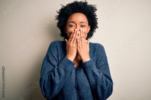 Young beautiful African American afro woman with curly hair wearing casual sweater laughing and embarrassed giggle covering mouth with hands, gossip and scandal concept photo