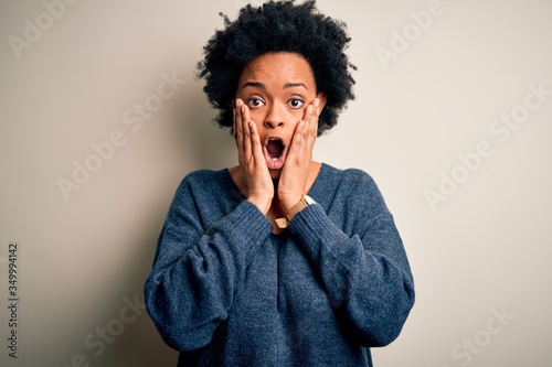 Young beautiful African American afro woman with curly hair wearing casual sweater afraid and shocked  surprise and amazed expression with hands on face