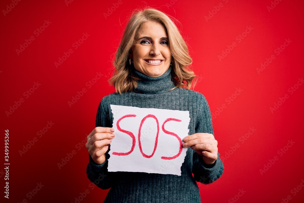 Middle age beautiful blonde woman holding paper with sos message over red bakground with a happy face standing and smiling with a confident smile showing teeth
