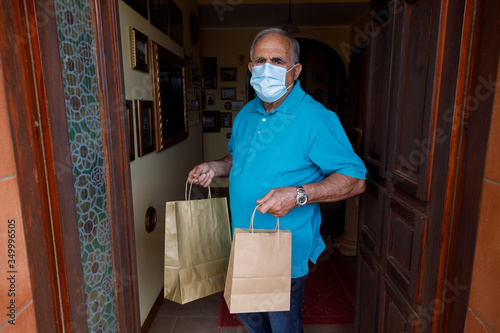 Anziano con mascherina e Polo azzurra è fermo sull'uscio di casa con le buste della spesa photo