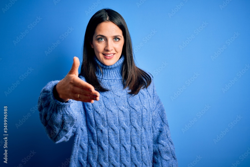 Young brunette woman with blue eyes wearing casual turtleneck sweater smiling friendly offering handshake as greeting and welcoming. Successful business. Young brunette woman with blue eyes wearing casual turtleneck sweater smiling friendly offering handshake as greeting and welcoming. Successful business.
