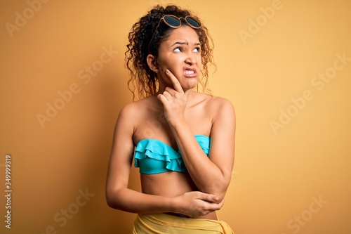 Young beautiful american woman on vacation wearing bikini over isolated yellow background Thinking worried about a question, concerned and nervous with hand on chin