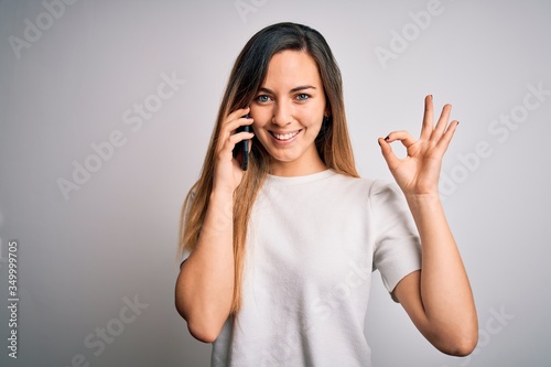 Young beautiful brunette woman having conversation talking on the smartphone doing ok sign with fingers, excellent symbol