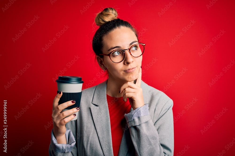 Young beautiful blonde businesswoman with blue eyes wearing glasses drinking cup of coffe serious face thinking about question, very confused idea Young beautiful blonde businesswoman with blue eyes wearing glasses drinking cup of coffe serious face thinking about question, very confused idea