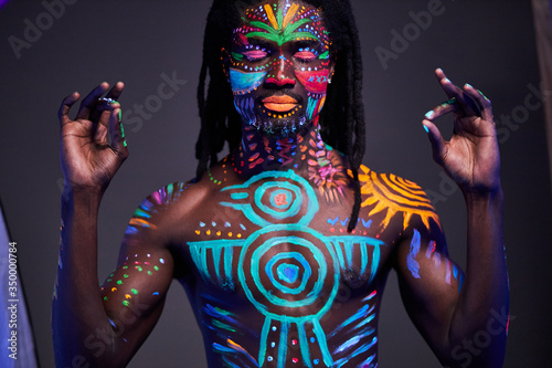 imperturbable man with UV body art practice meditation, show keep calm gesture at camera. yoga, calmness, luminescence, fluorescence concept