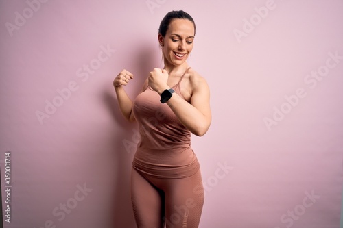 Young blonde fitness woman wearing sport workout clothes over pink isolated background showing arms muscles smiling proud. Fitness concept.