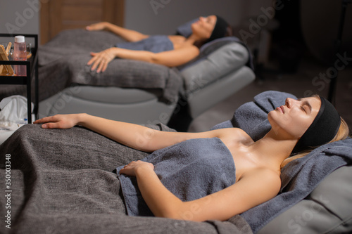 two young attractive female lie on bed in towels before face lift procedure, women came to get beauty procedures. relaxation. skincare and wellbeing concept