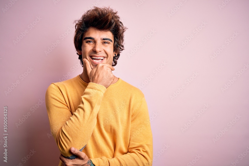 Young handsome man wearing yellow casual t-shirt standing over isolated pink background looking confident at the camera smiling with crossed arms and hand raised on chin. Thinking positive. Young handsome man wearing yellow casual t-shirt standing over isolated pink background looking confident at the camera smiling with crossed arms and hand raised on chin. Thinking positive.