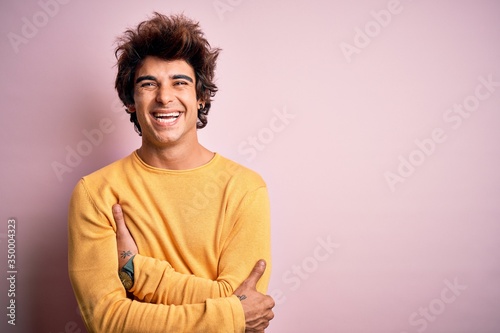 Young handsome man wearing yellow casual t-shirt standing over isolated pink background happy face smiling with crossed arms looking at the camera. Positive person.