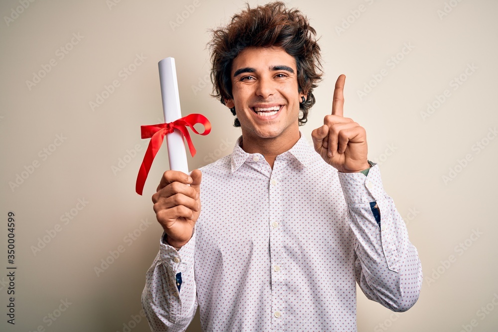 Young handsome student man holding diploma standing over isolated pink background surprised with an idea or question pointing finger with happy face, number one Young handsome student man holding diploma standing over isolated pink background surprised with an idea or question pointing finger with happy face, number one