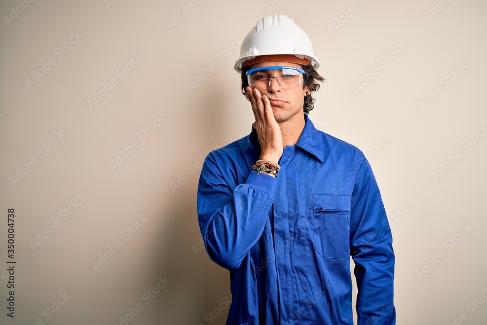 Young constructor man wearing uniform and security helmet over isolated white background thinking looking tired and bored with depression problems with crossed arms.