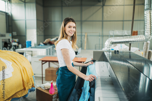 Young laundry worker pats the linen on the automatic machine at the dry cleaners.